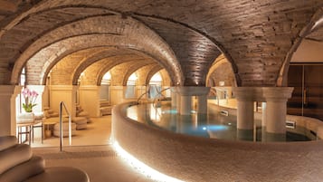 Ein Wellnessbereich mit einem Steinbecken, Gewölbedecken und Sitzgelegenheiten.