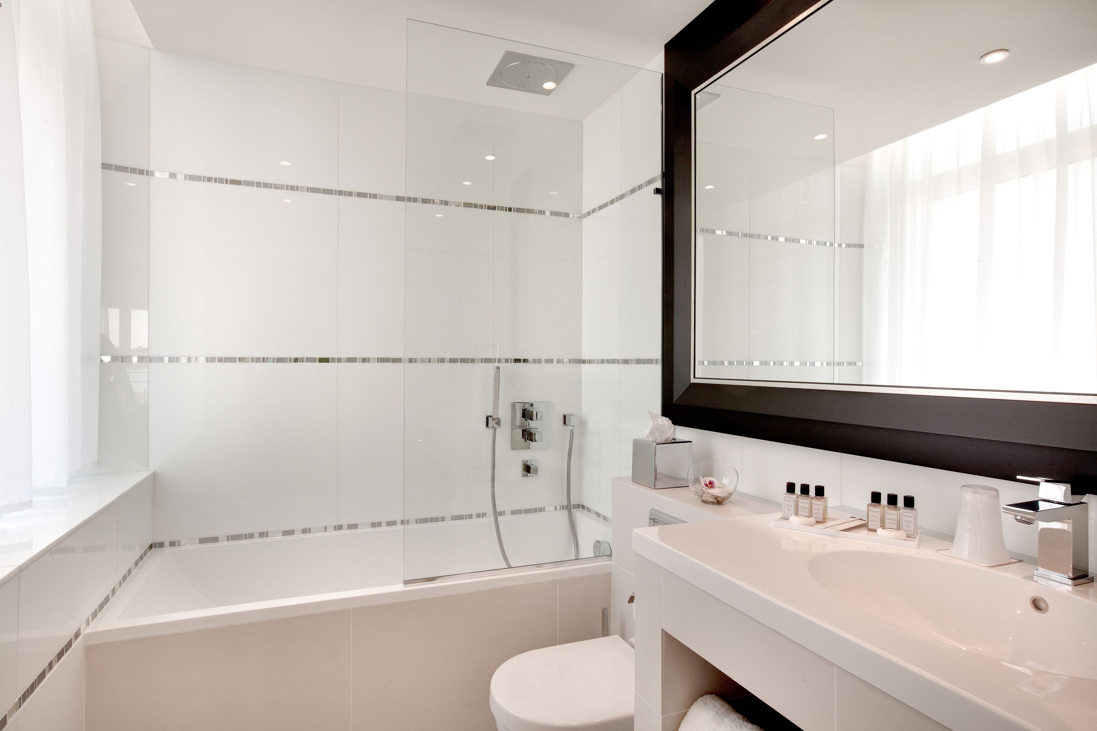 A modern bathroom with a glass-enclosed shower, a white sink with toiletries, and a large mirror.