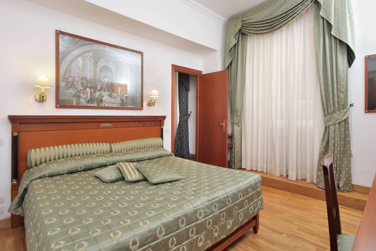A hotel room with a large bed, a wooden headboard, a painting above the bed, and a door leading to another room.