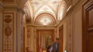 A hallway with ornate ceiling decorations, wooden flooring, and a desk with a computer. - Relais Pierret (Rome)