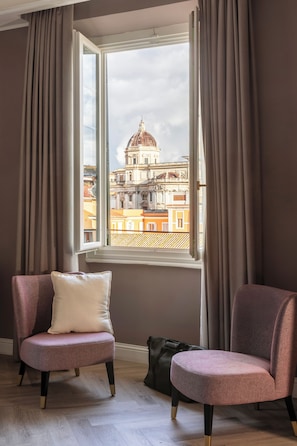 A room with two chairs, a window with curtains, and a view of a building with a dome.