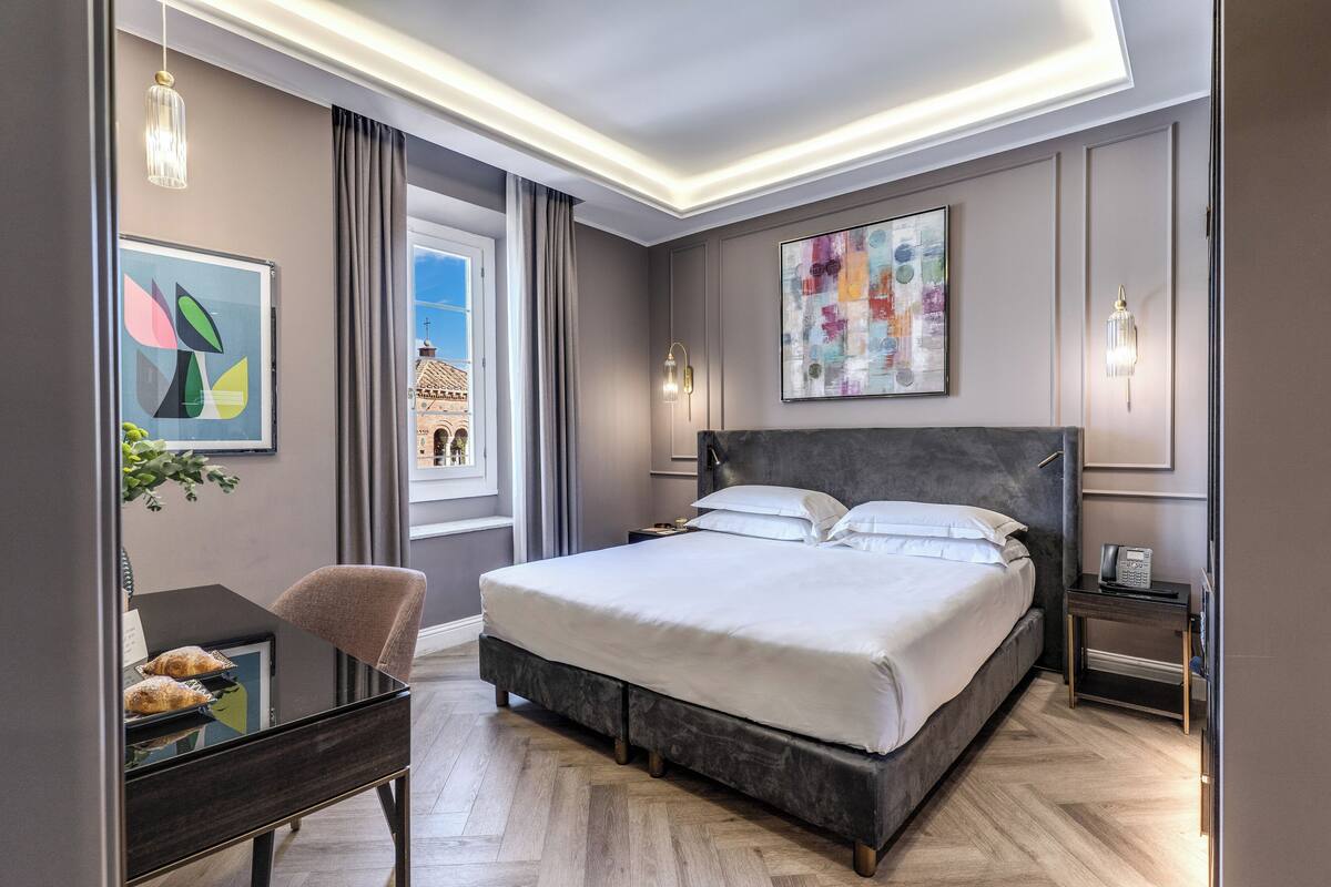 A modern hotel room with a large bed, a desk, and a view of the cityscape.
