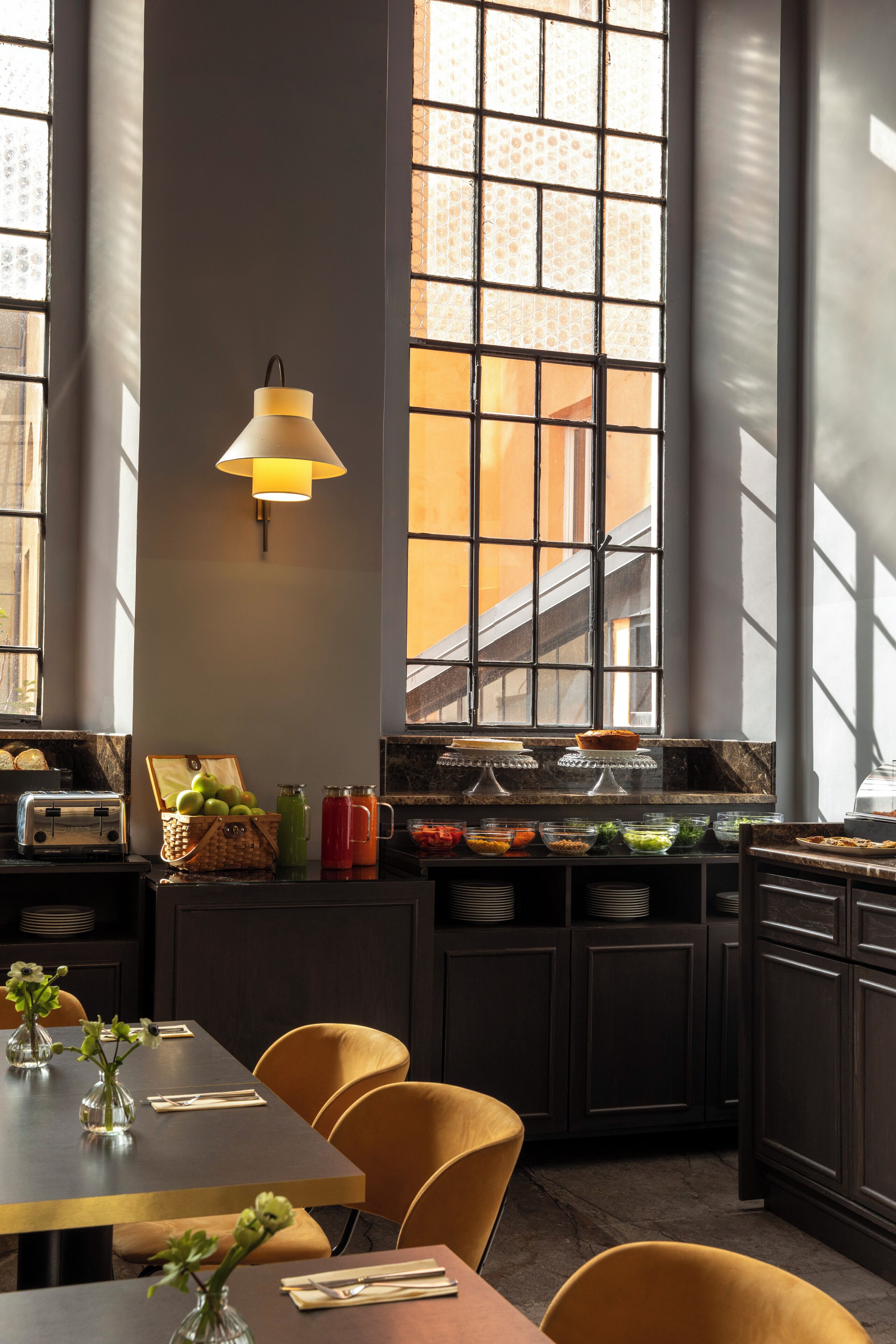 A modern dining area with a long table, chairs, a buffet with various food items, and a large window with a view of the outside.