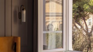 A hotel room with a bed, bedside table, lamp, and a window with a view of a building and trees. - Hotel Viminale (Rome)