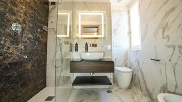A bathroom with a glass-enclosed shower, a marble sink, and a toilet.