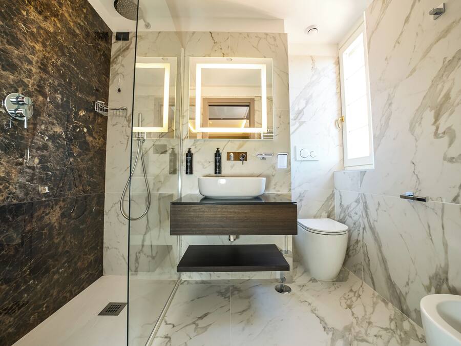 A bathroom with a glass-enclosed shower, a marble sink, and a toilet.