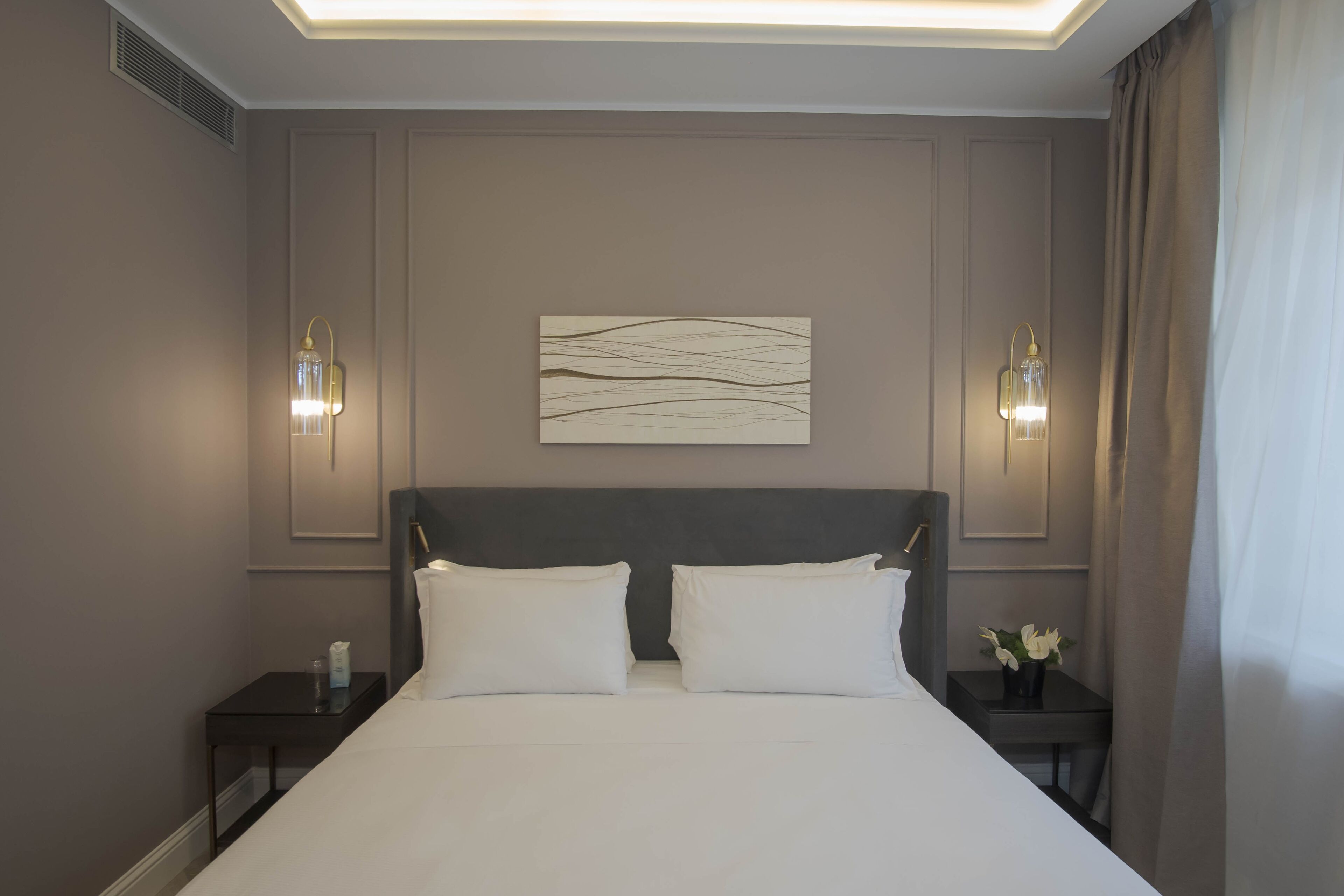Une chambre d’hôtel avec un grand lit, deux tables de chevet, une œuvre d’art accrochée au mur et deux appliques murales.