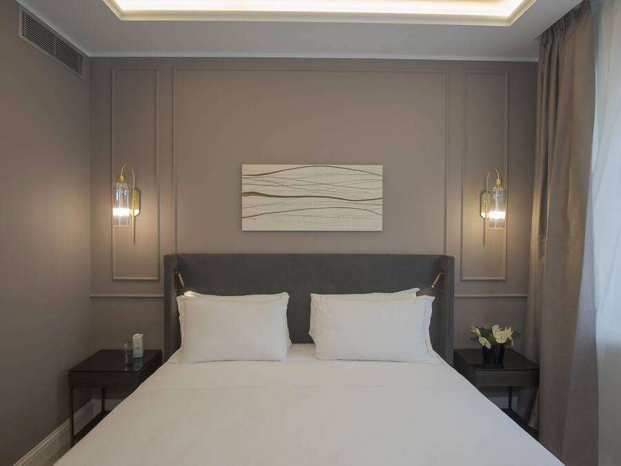 Une chambre d’hôtel avec un grand lit, deux tables de chevet, une œuvre d’art accrochée au mur et deux appliques murales.