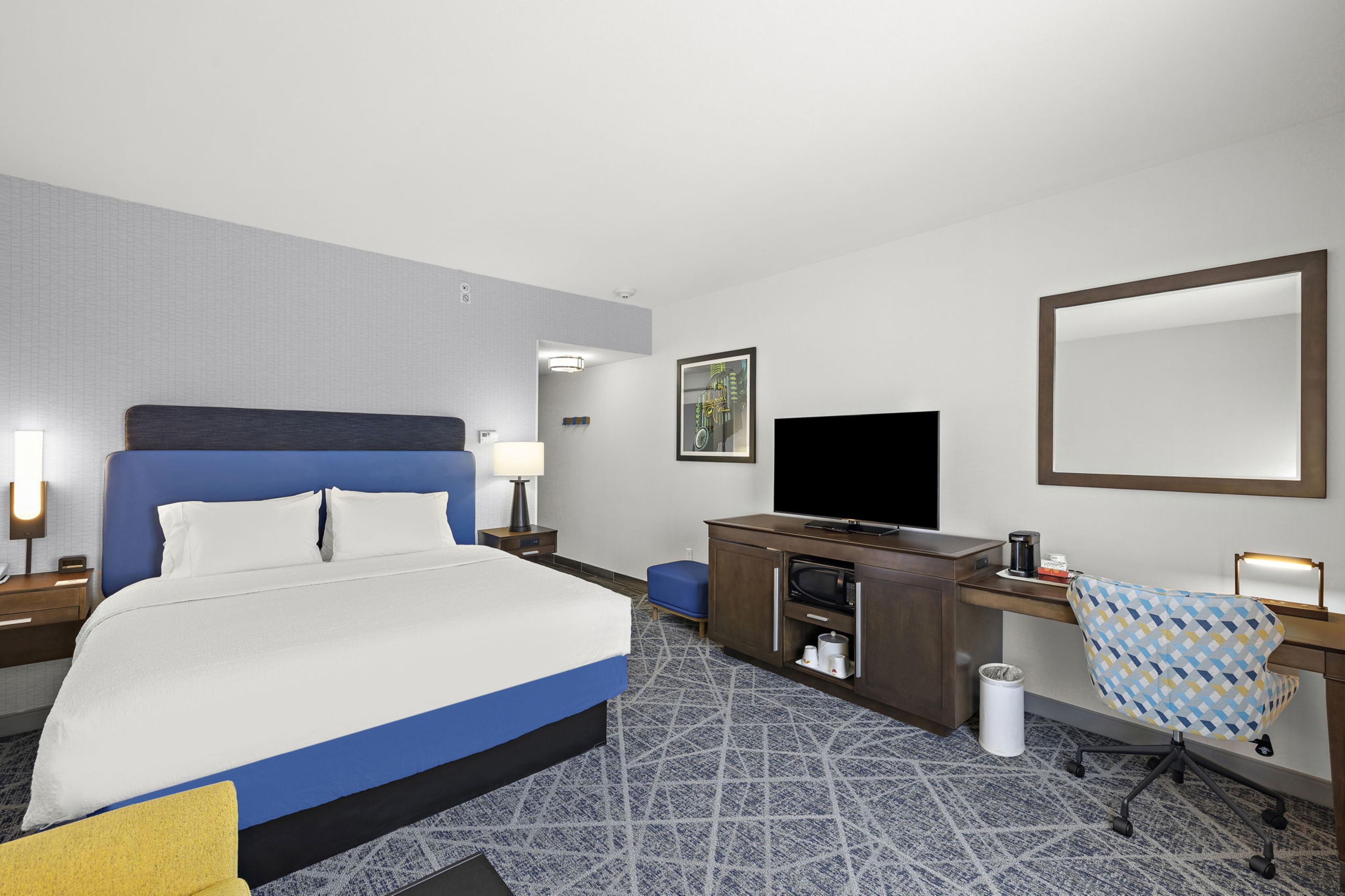 A hotel room with a large bed, a desk, a television, and a chair.