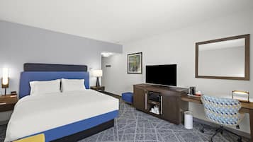 A hotel room with a large bed, a desk, a television, and a chair.