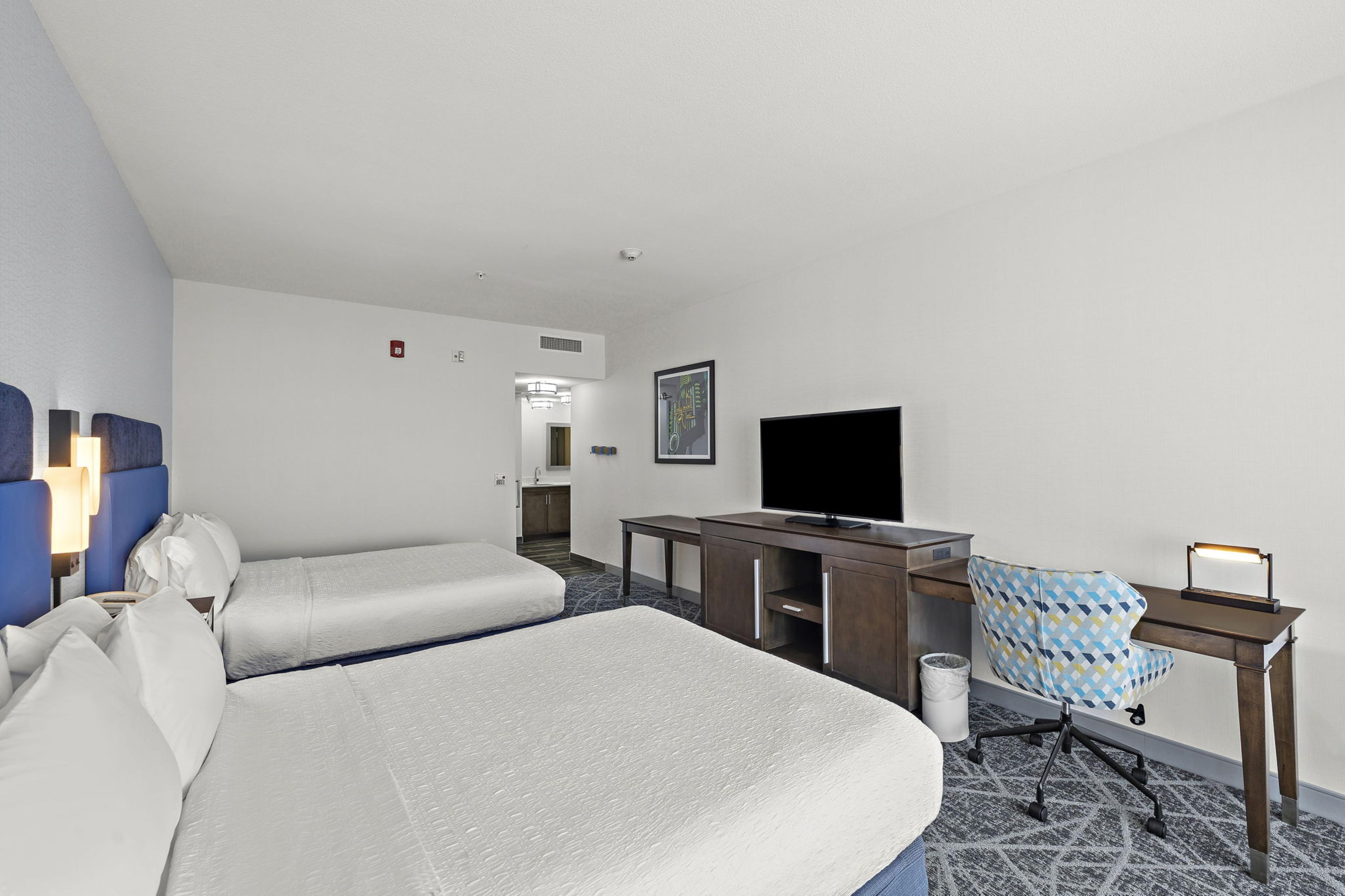 Une chambre d’hôtel avec deux lits, un bureau avec un ordinateur, une télévision et une chaise.