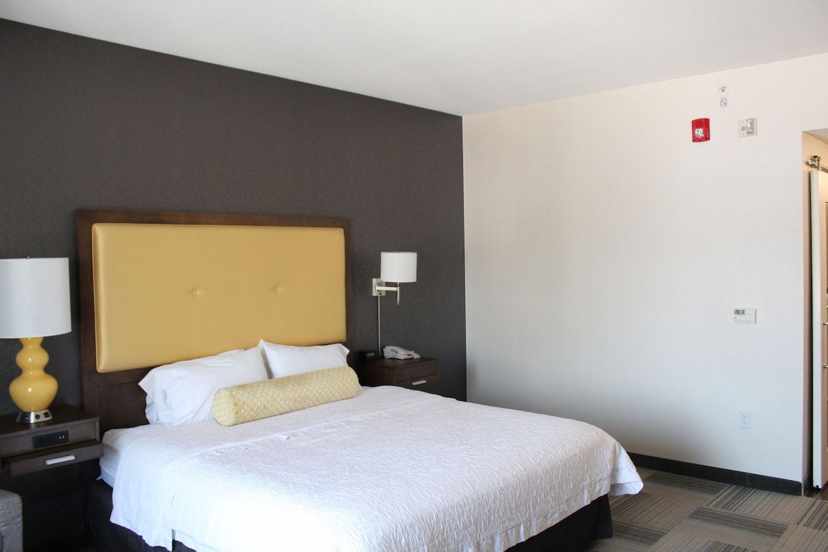 A hotel room with a large bed, a bedside table with a lamp, a nightstand, and a wall-mounted phone.