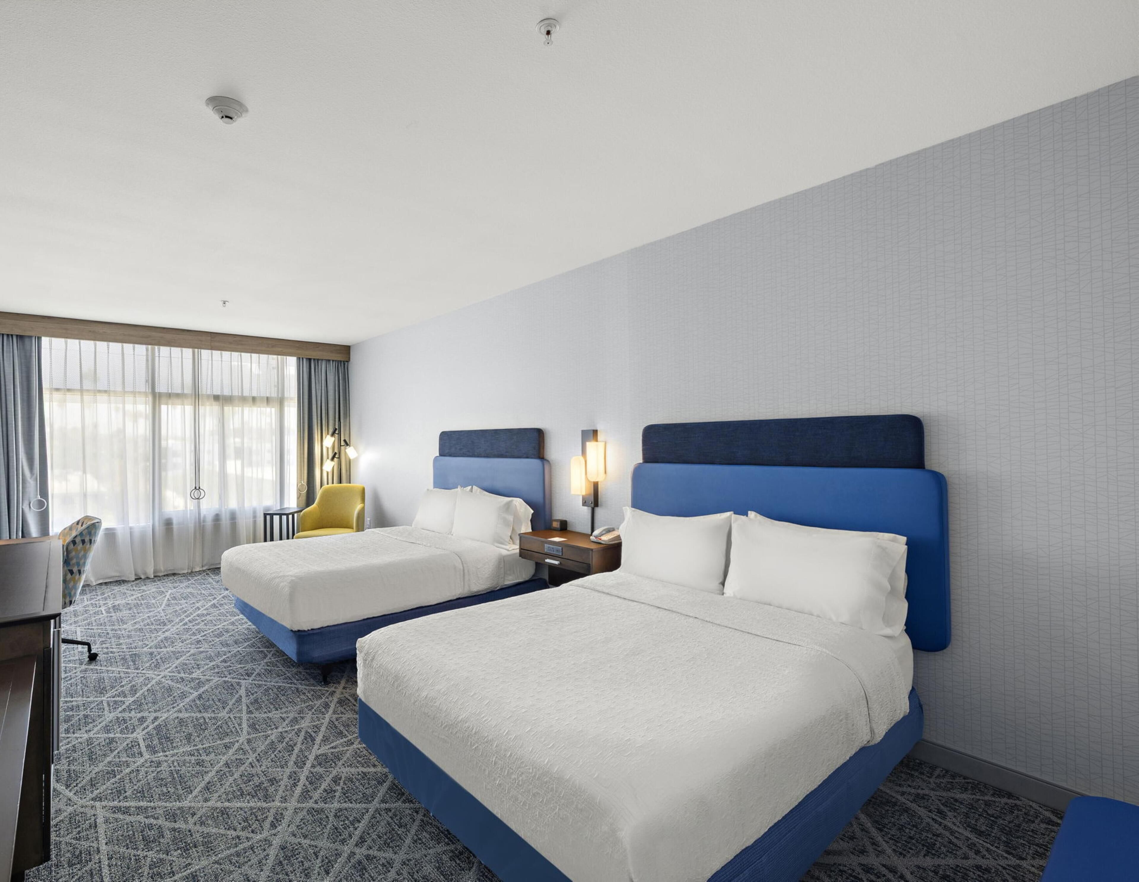 Ein Hotelzimmer mit zwei Betten, einem Schreibtisch, einem Stuhl und einem Fenster mit Vorhängen.
