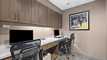 Un espace de bureau moderne avec un grand bureau, deux chaises, une imprimante et un tableau encadré accroché au mur.