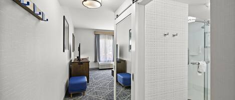 A hotel room with a modern design, including a shower area, a seating area with a blue chair, and a small desk.