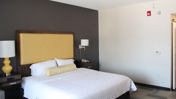 A hotel room with a large bed, a nightstand with a lamp, and a door to the right. - Hampton Inn & Suites Los Angeles/Hollywood (Los Angeles)