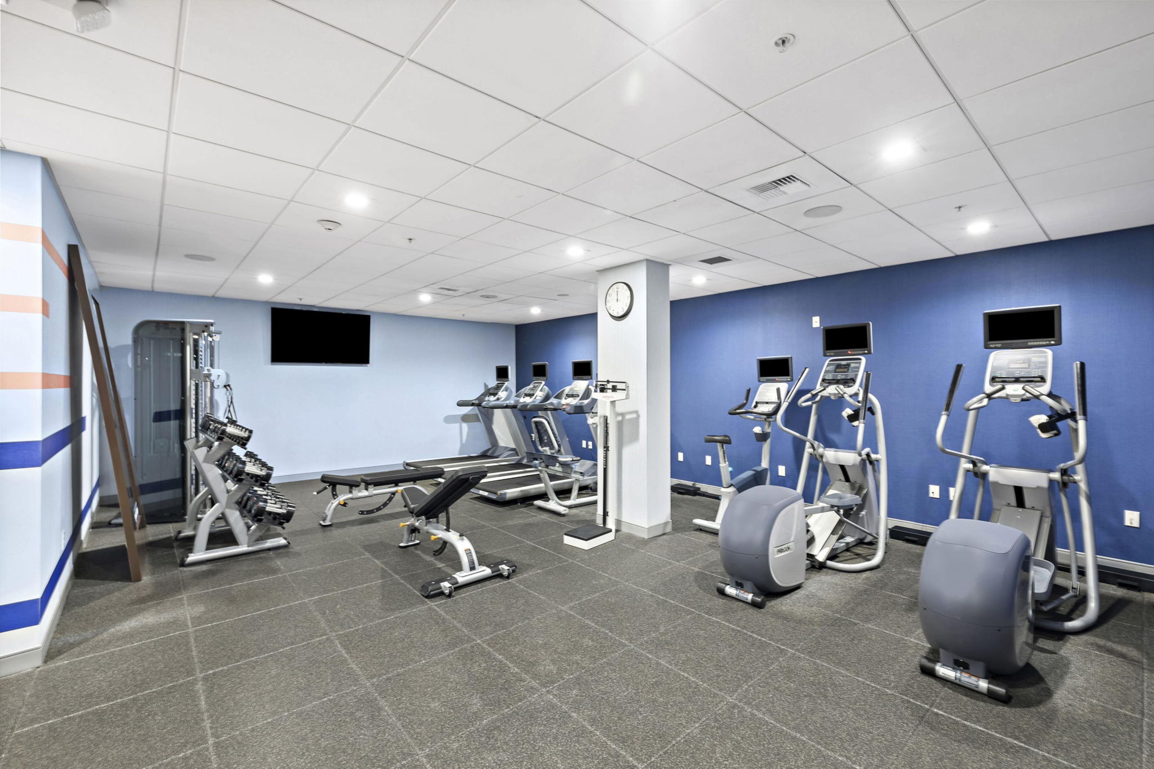 A gym with various exercise equipment, a clock, and a blue wall.