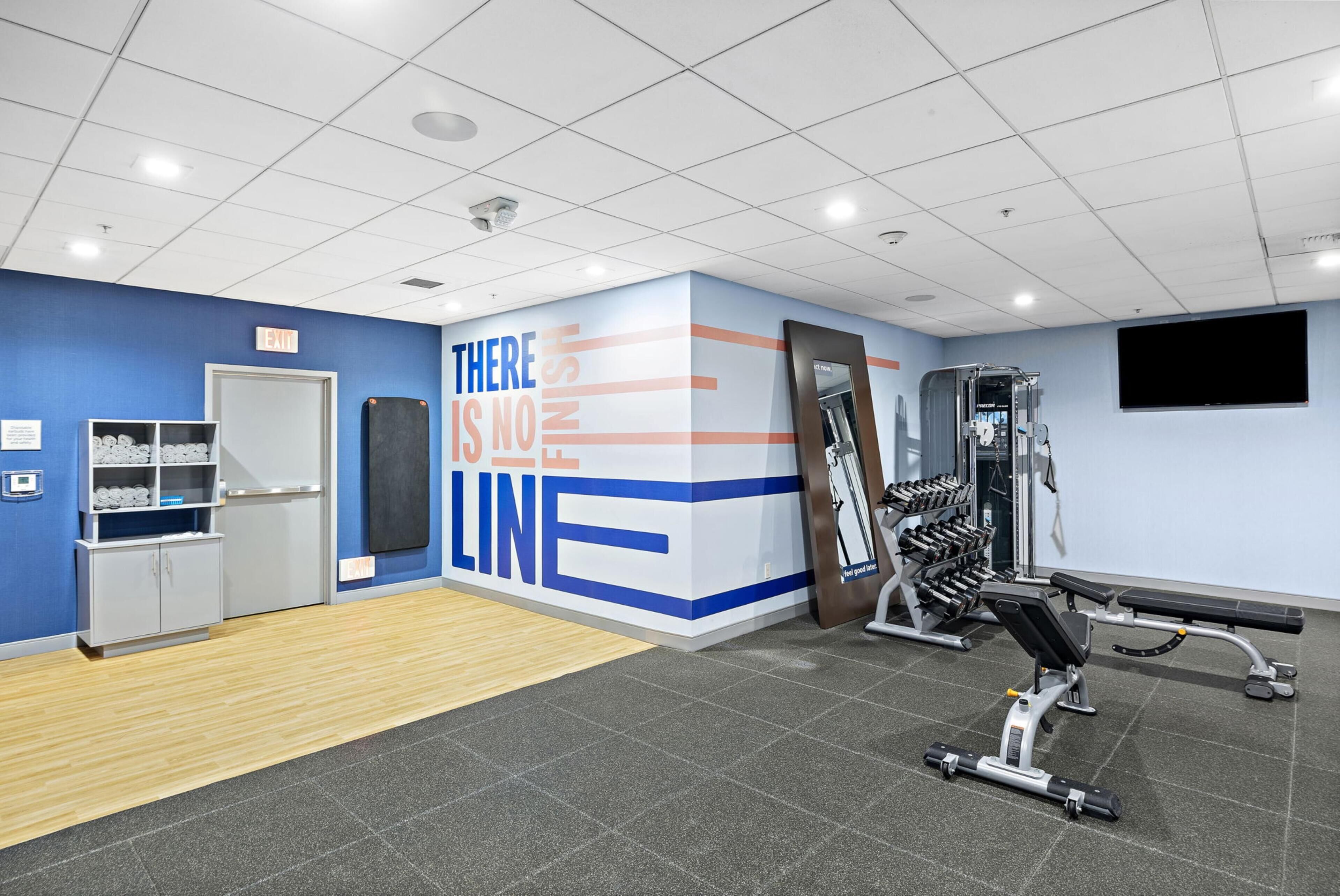 Une salle de sport équipée de matériel d’exercice, un mur orné de messages motivants et un panneau indiquant la sortie.