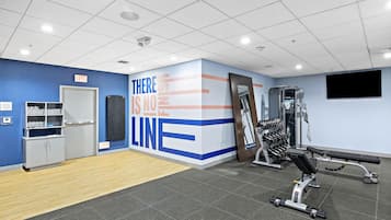 Une salle de sport équipée de matériel d’exercice, un mur orné de messages motivants et un panneau indiquant la sortie.