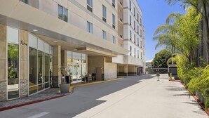 A modern hotel entrance with a covered walkway, large windows, and a parking area. - Hampton Inn & Suites Los Angeles/Hollywood (Los Angeles)