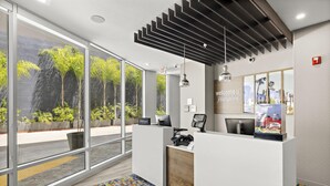 A hotel reception area with a modern design, including a reception desk, a 'Welcome to Hampton' sign, and a view of the outdoors through large windows. - Hampton Inn & Suites Los Angeles/Hollywood (Los Angeles)