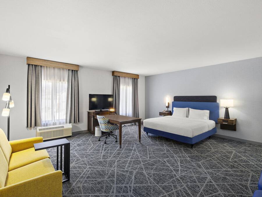 A hotel room with a bed, desk, chair, and a television.
