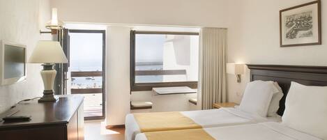 Habitación de hotel con dos camas, un escritorio, una lámpara, un televisor y vista a la playa.