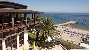 A beachside hotel with a balcony overlooking the sea, a palm tree, and beach umbrellas. - Hotel Do Mar (Sesimbra)
