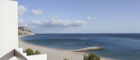 A coastal view with a beach, rocky cliffs, and a clear sky.