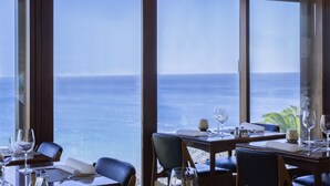 A dining area with tables set for two, overlooking a view of the sea. - Hotel Do Mar (Sesimbra)