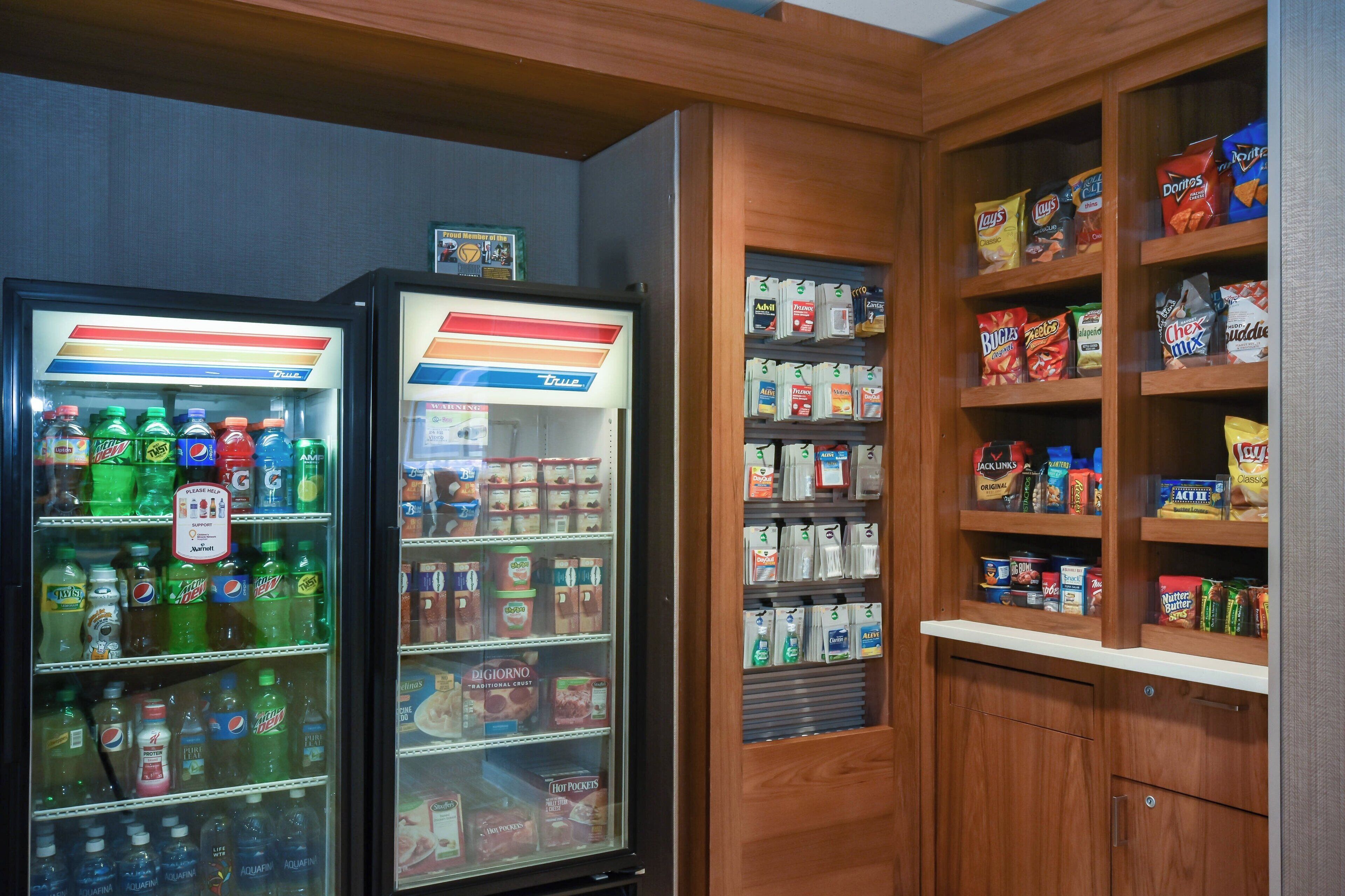 Un distributeur automatique proposant diverses boissons et collations, un réfrigérateur rempli de boissons, et des étagères garnies de collations et d’aliments.