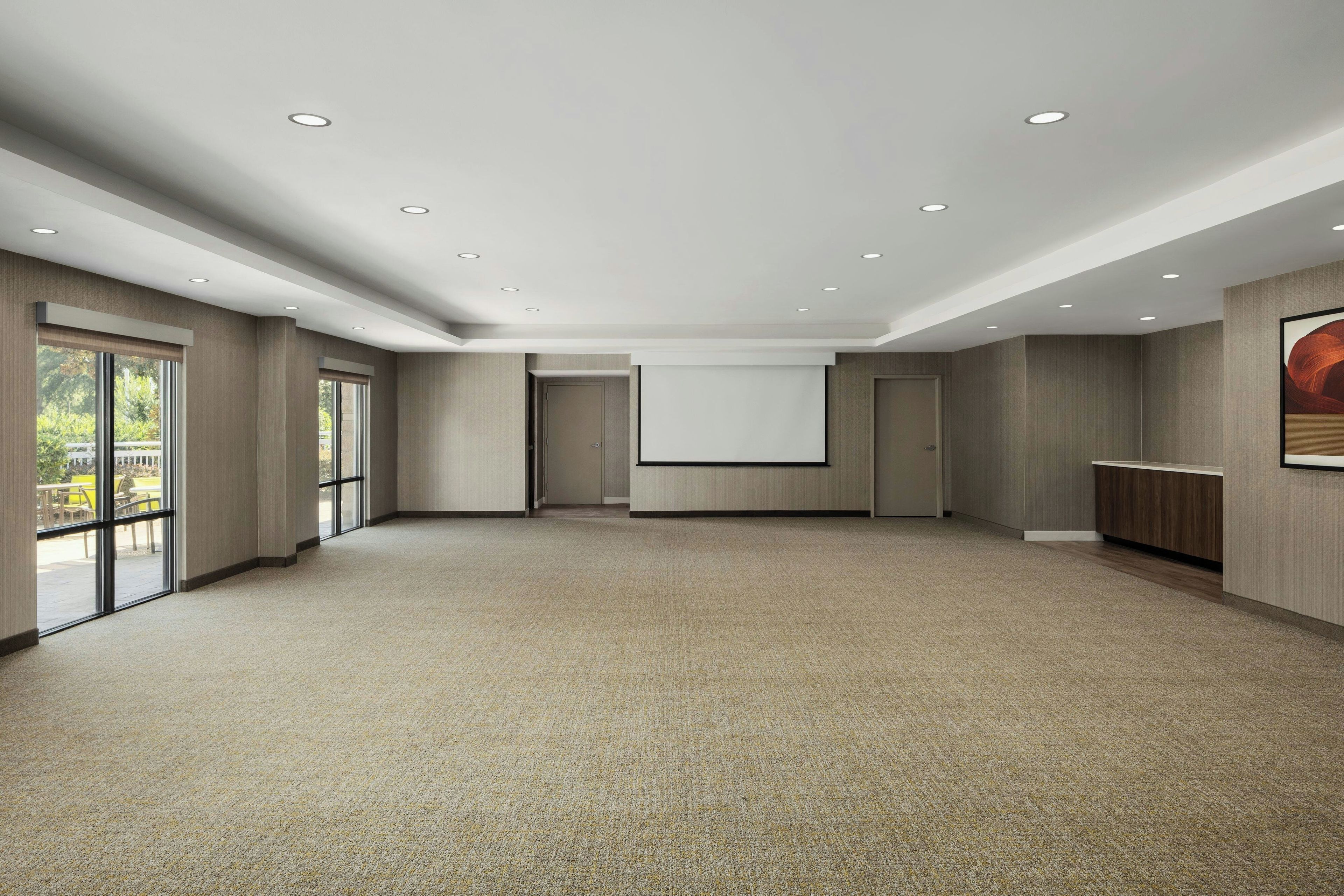 A spacious room with carpeted flooring, a large projection screen, and a door leading to another area.