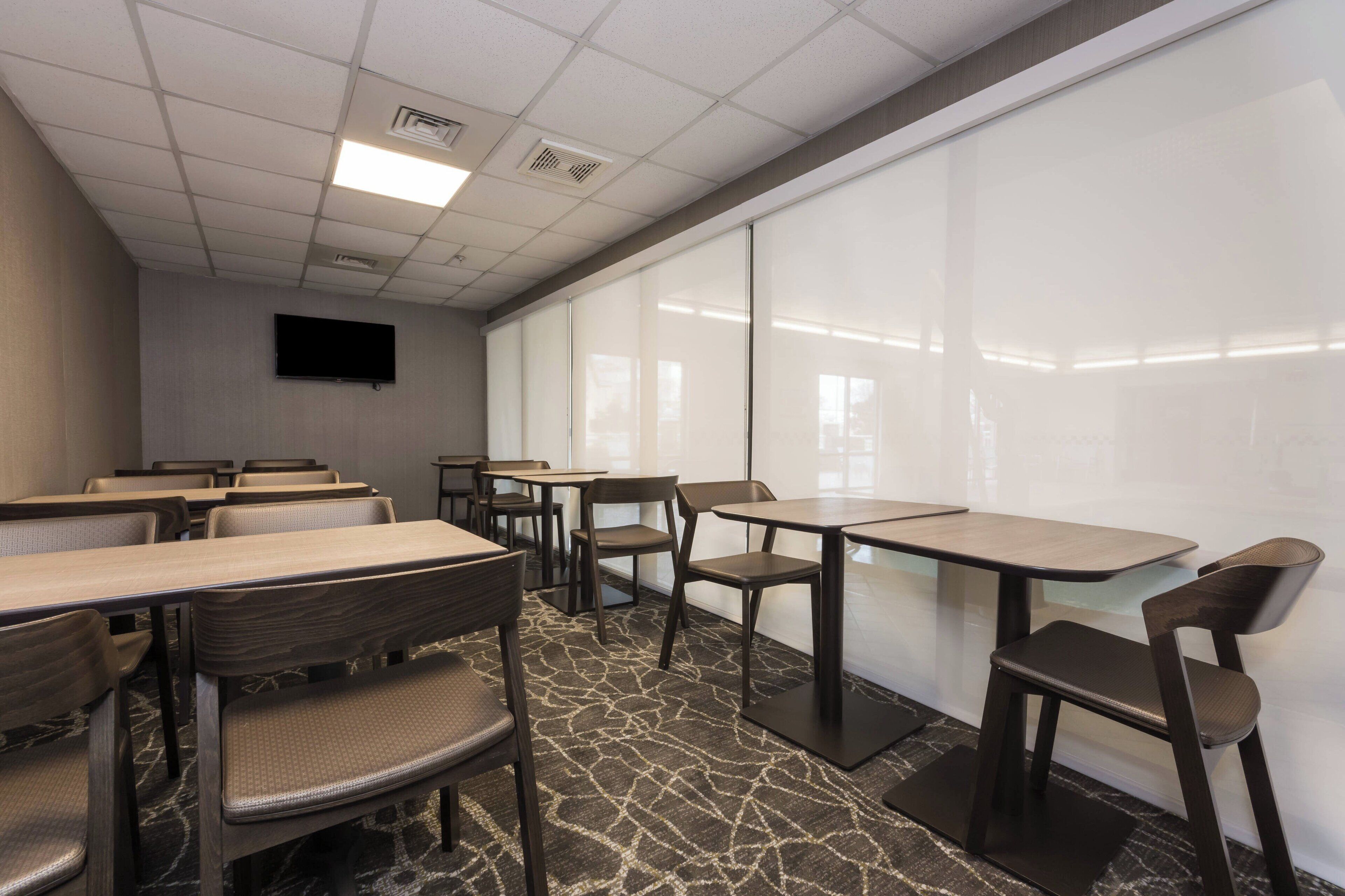 A conference room with tables and chairs, a flat-screen TV, and a patterned carpet.
