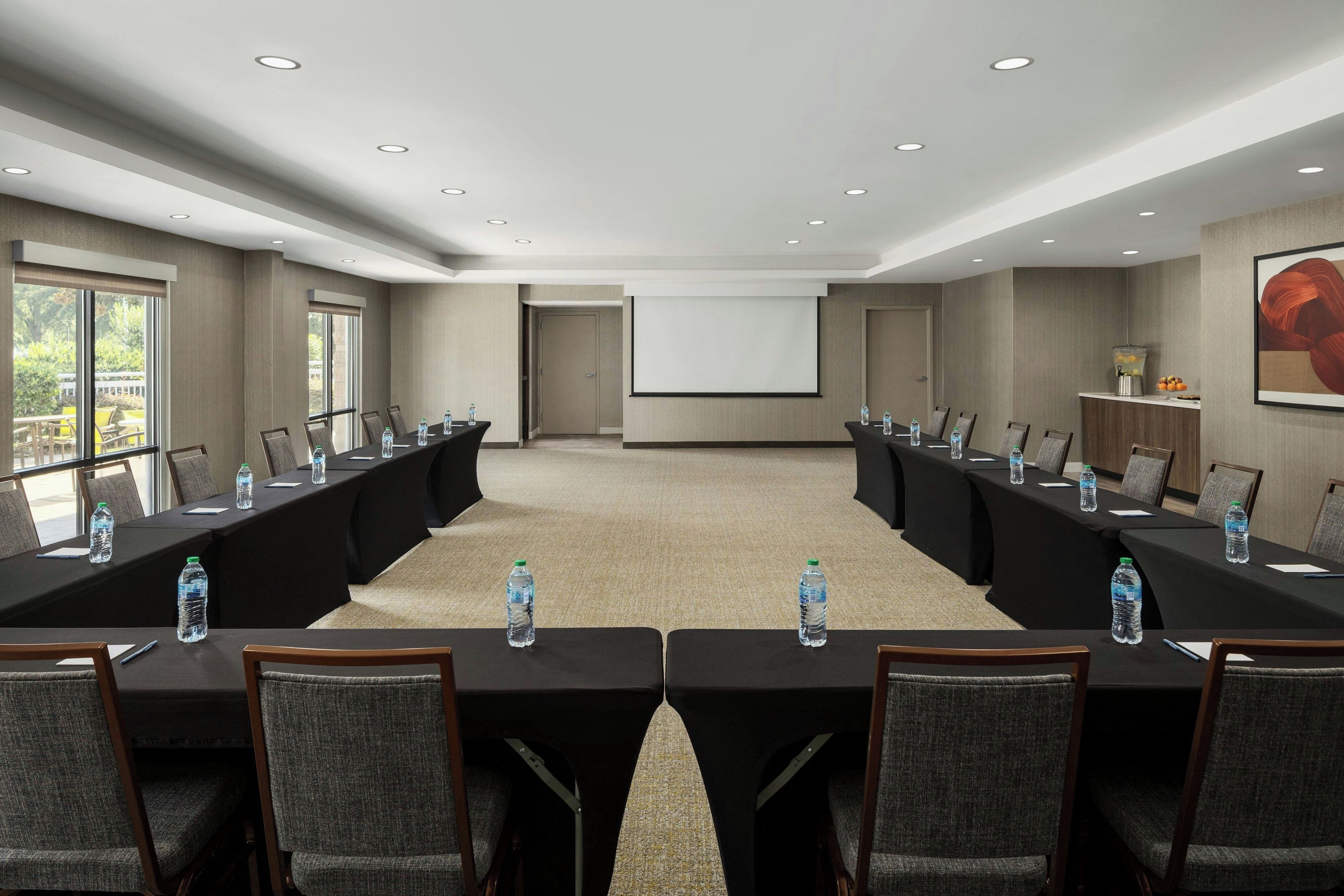 A conference room with a long table, chairs, a projector screen, and water bottles.