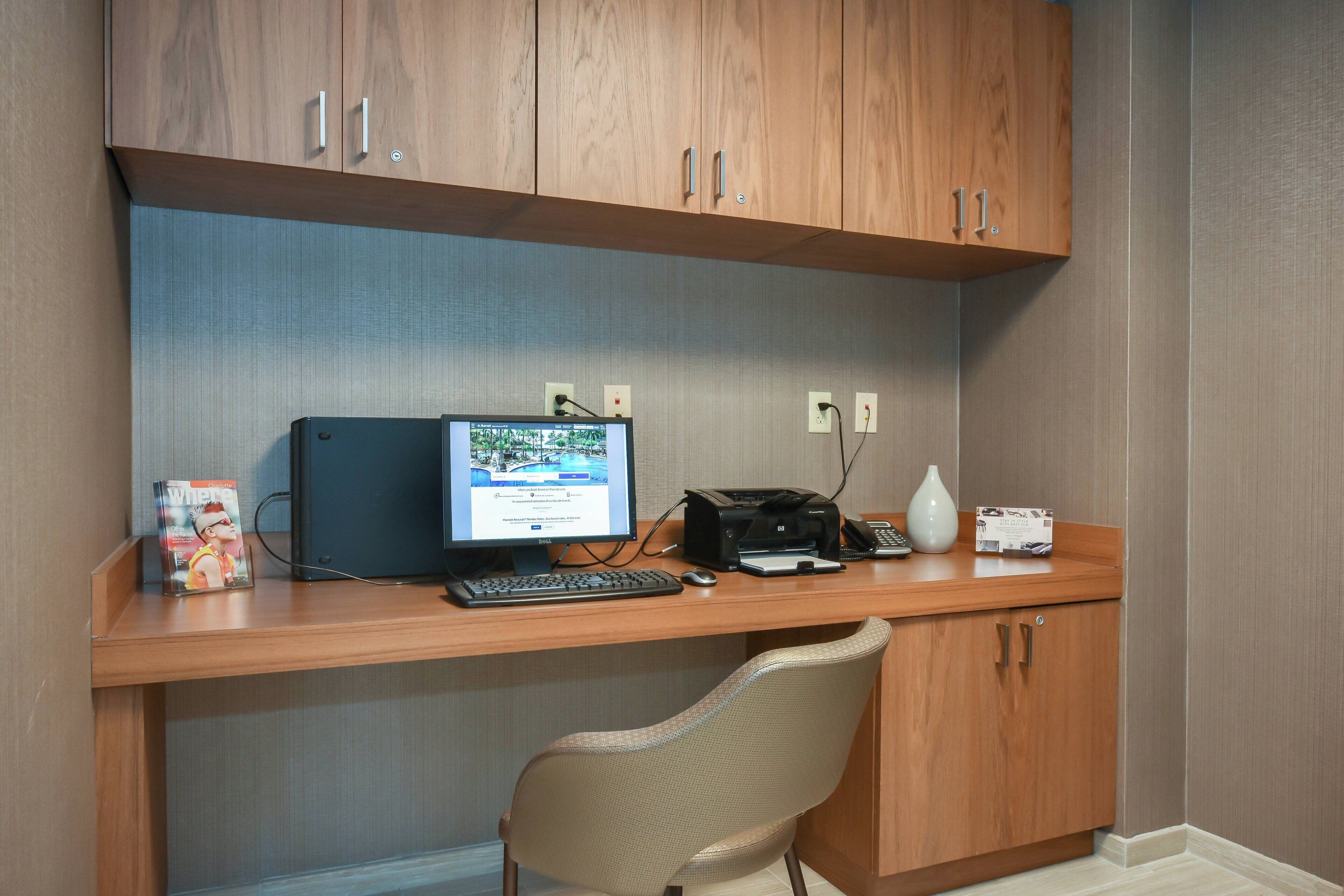 A wooden desk with a computer, keyboard, mouse, and printer. There is a chair in front of the desk.