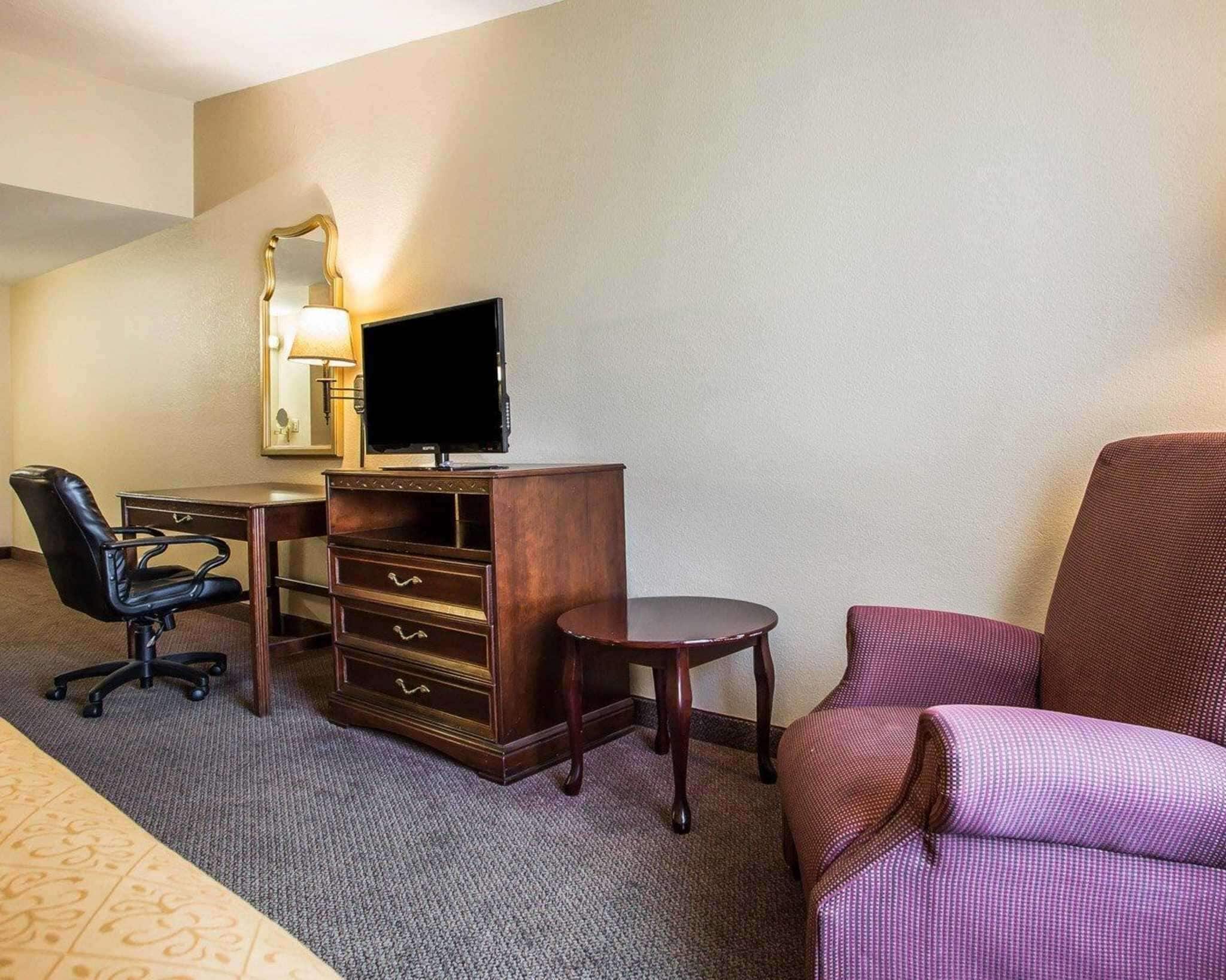A hotel room with a desk, a chair, a television, a mirror, and a bed.