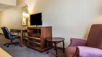 A hotel room with a desk, a chair, a television, a mirror, and a bed.