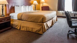 Une chambre d’hôtel avec un grand lit, deux lampes de chevet, une chaise, un bureau et une fenêtre avec des rideaux.