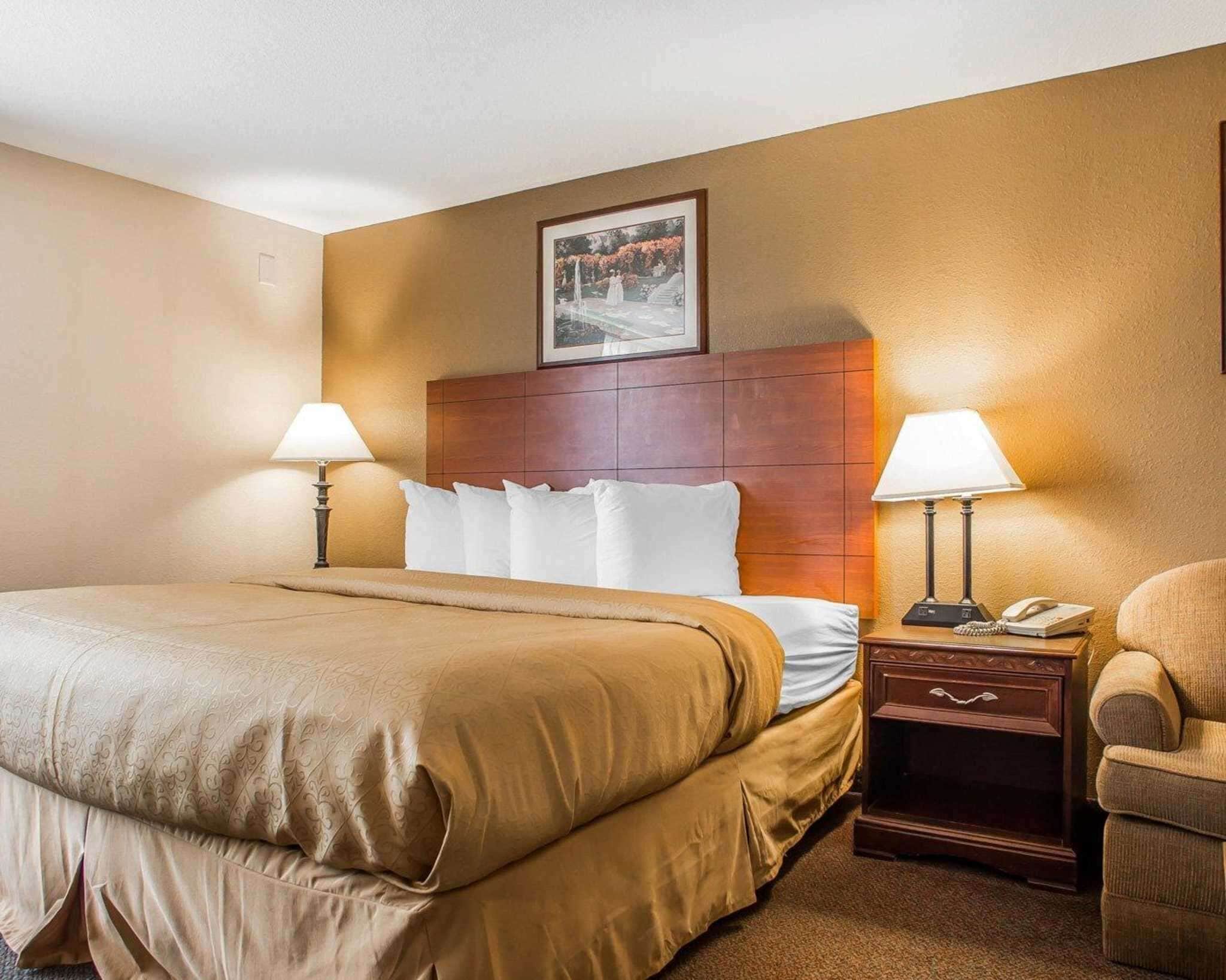 A hotel room with a large bed, two bedside tables with lamps, a chair, and a framed picture on the wall.