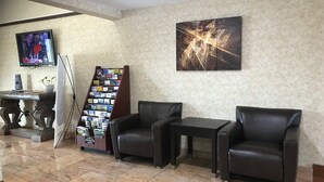 Un hall d’entrée avec deux fauteuils en cuir, une petite table, une bibliothèque, un téléviseur et un grand tableau abstrait accroché au mur.