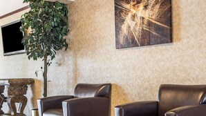 Un hall d’entrée avec deux fauteuils en cuir, une grande plante en pot, un téléviseur fixé au mur et une œuvre d’art abstraite.