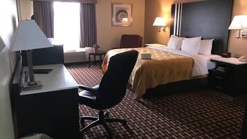 A hotel room with a bed, desk, chair, lamps, and a clock.