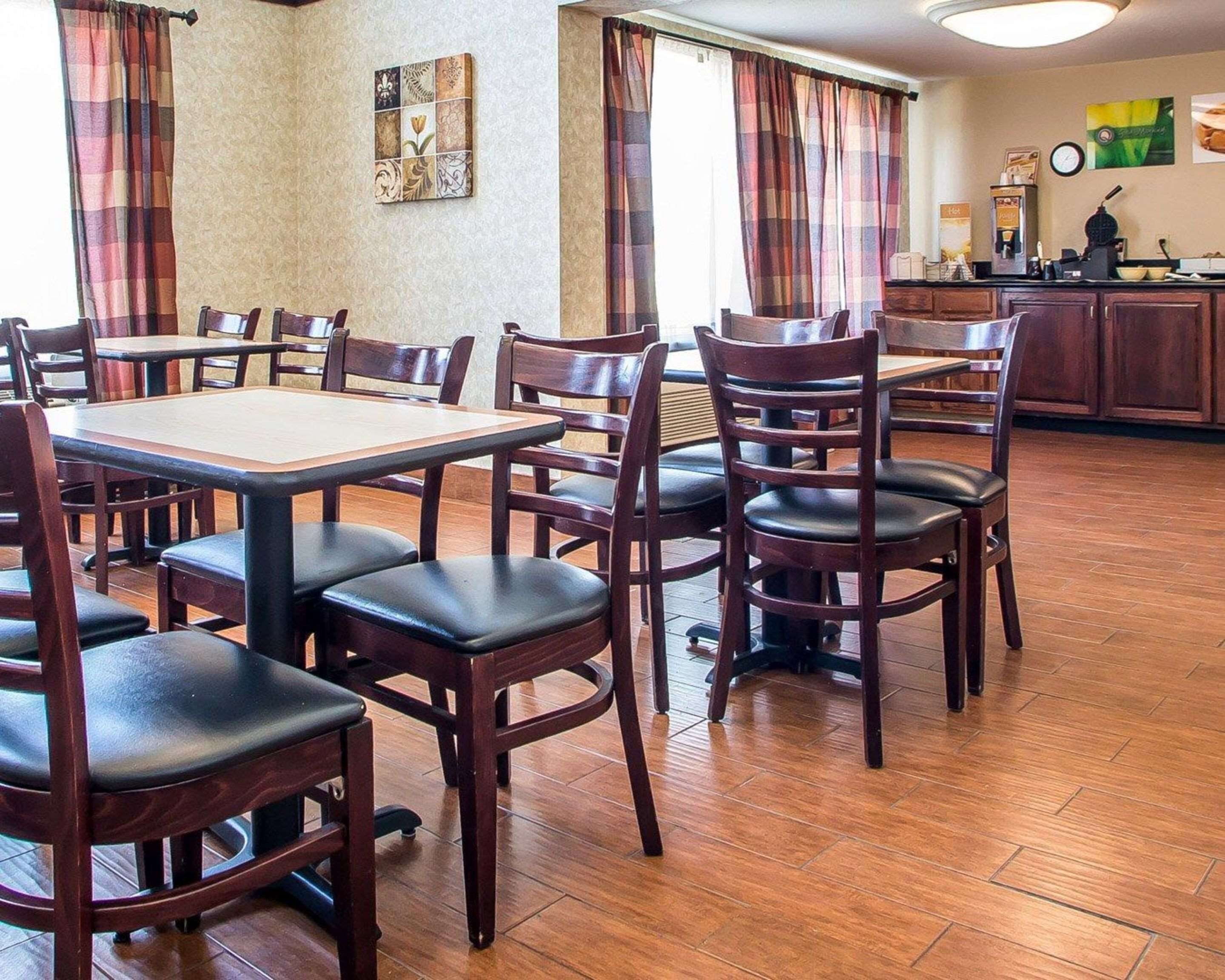 A dining area with wooden tables and chairs, a kitchen area with a coffee machine, and a clock on the wall.