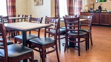 A dining area with wooden tables and chairs, a kitchen area with a coffee machine, and a clock on the wall.