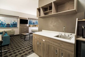 A modern kitchen with a built-in sink, wooden cabinets, and a flat-screen TV mounted above the counter.