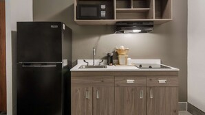 Une cuisine compacte avec un réfrigérateur noir, des placards en bois, un four à micro-ondes et un four encastré.