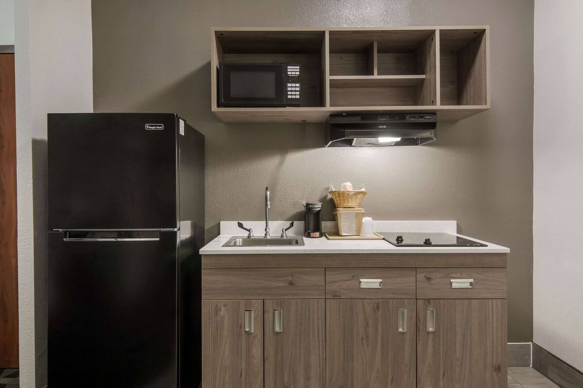 A compact kitchen with a black refrigerator, wooden cabinets, a microwave, and a built-in oven.