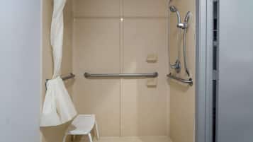 A small, enclosed shower area with a white shower chair, grab bars, and a showerhead.