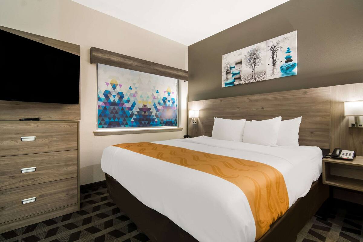 A hotel room with a large bed, a flat-screen TV, a nightstand, and artwork on the walls.