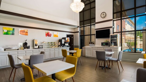 Un restaurant moderne doté d’un haut plafond, de grandes fenêtres et de différents types de sièges, notamment des chaises jaunes et des tables blanches.